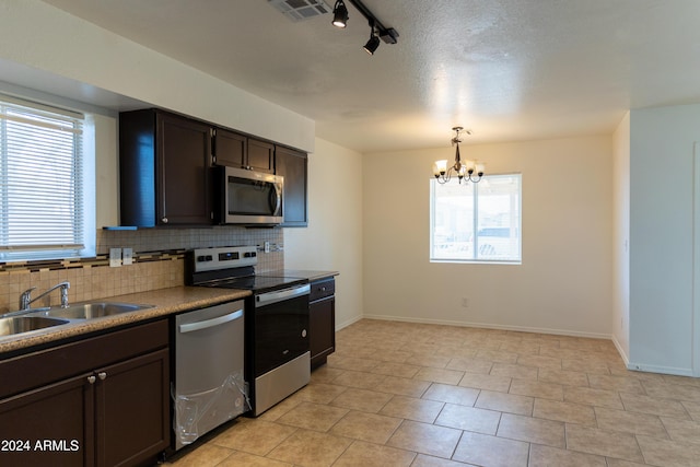 kitchen featuring an inviting chandelier, rail lighting, sink, decorative backsplash, and stainless steel appliances