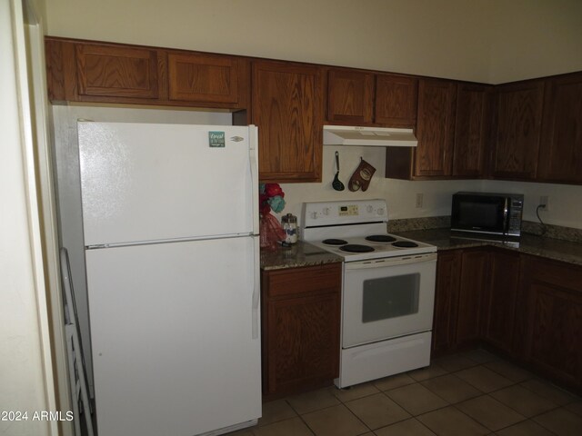 kitchen featuring dark stone counters, white appliances, and light tile patterned floors