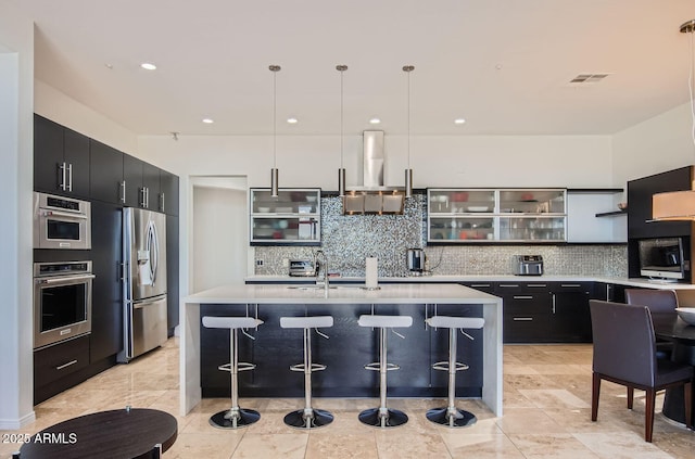 kitchen with hanging light fixtures, tasteful backsplash, a kitchen bar, a center island with sink, and appliances with stainless steel finishes