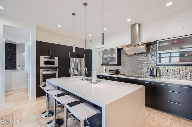 kitchen featuring a kitchen breakfast bar, wall chimney range hood, an island with sink, and stainless steel appliances