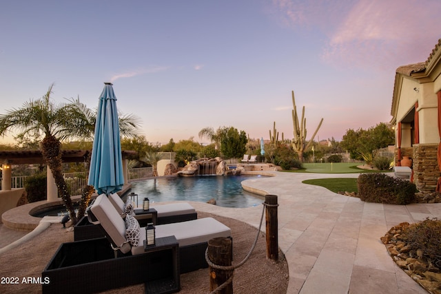 pool at dusk with a patio area, pool water feature, and an in ground hot tub