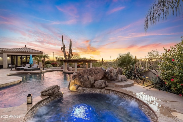 pool at dusk with a jacuzzi, pool water feature, and a patio area