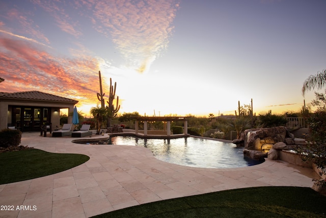 pool at dusk with pool water feature and a patio area