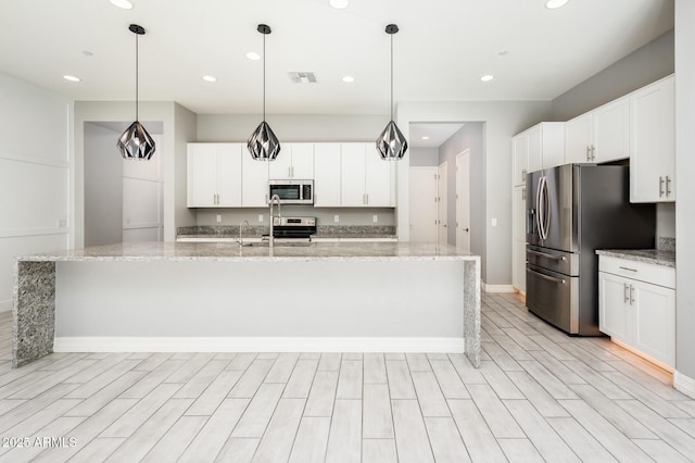 kitchen with white cabinets, visible vents, appliances with stainless steel finishes, light stone counters, and a center island with sink
