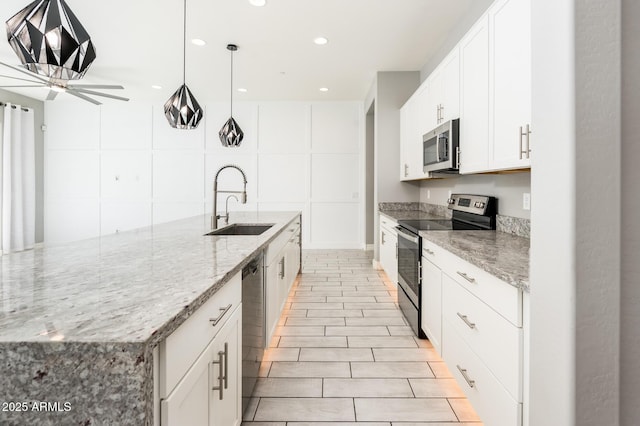 kitchen featuring a ceiling fan, white cabinets, appliances with stainless steel finishes, light stone counters, and a sink