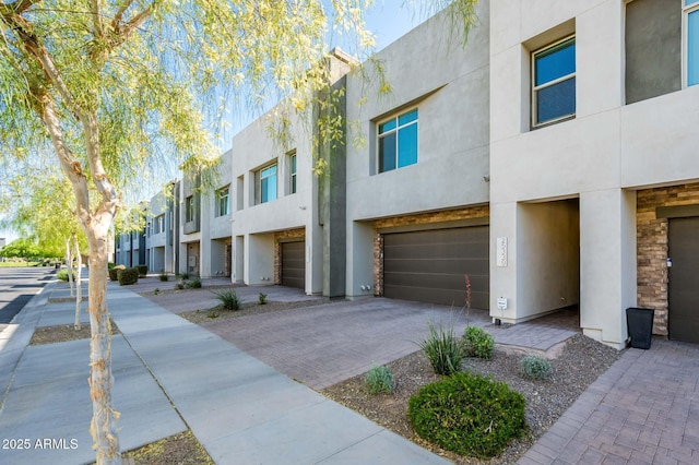 view of front of house with a garage, stucco siding, a residential view, and decorative driveway