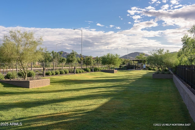 view of property's community featuring a mountain view, a vegetable garden, fence, and a lawn