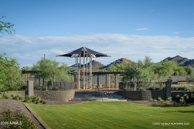 community jungle gym with a mountain view, fence, and a lawn