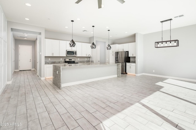 kitchen featuring visible vents, baseboards, appliances with stainless steel finishes, and a kitchen island with sink