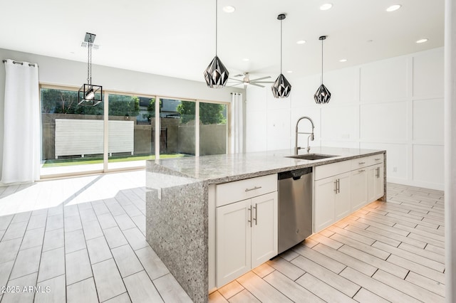 kitchen featuring white cabinets, light stone countertops, stainless steel dishwasher, a decorative wall, and a sink