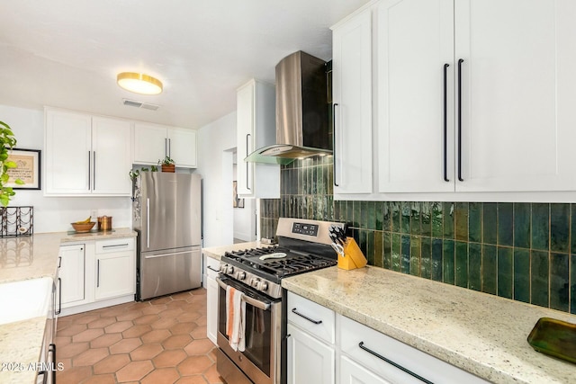 kitchen featuring white cabinetry, stainless steel appliances, light stone counters, and wall chimney range hood