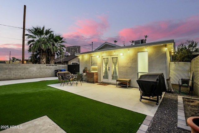 back house at dusk featuring a patio, a lawn, and french doors