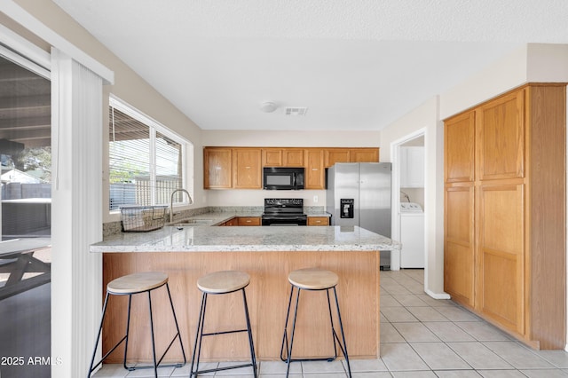 kitchen with a peninsula, a sink, visible vents, black appliances, and washer / clothes dryer