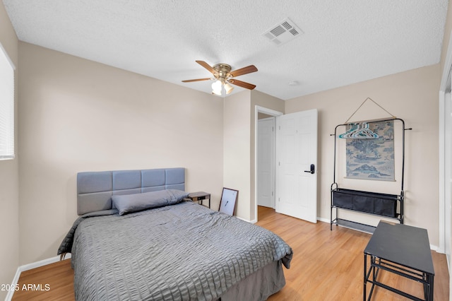 bedroom featuring light wood-type flooring, baseboards, visible vents, and a textured ceiling