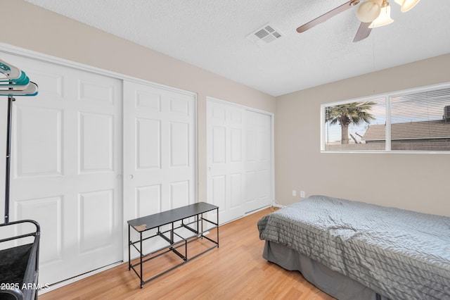 bedroom with light wood-type flooring, a ceiling fan, visible vents, and a textured ceiling