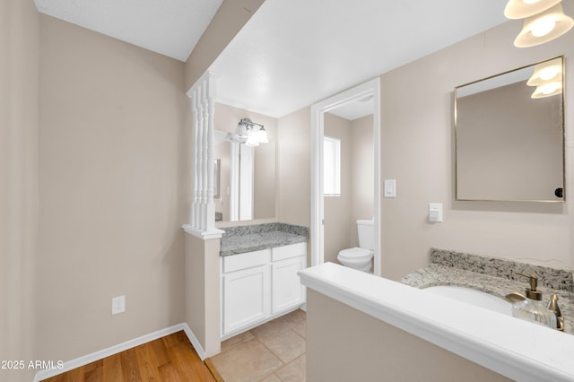 bathroom featuring two vanities, toilet, a sink, wood finished floors, and baseboards