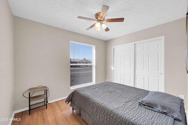 bedroom with baseboards, a ceiling fan, wood finished floors, a textured ceiling, and a closet