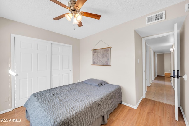 bedroom featuring baseboards, visible vents, light wood-style flooring, a textured ceiling, and a closet