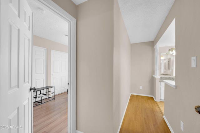 hall with light wood-style floors, a textured ceiling, and baseboards