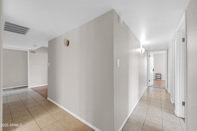 corridor featuring baseboards, visible vents, and light tile patterned flooring