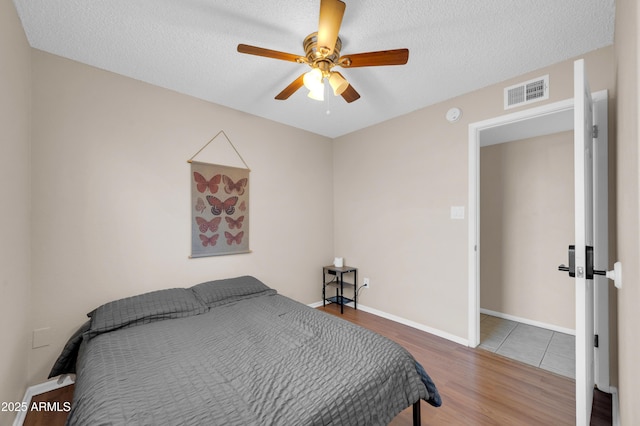 bedroom with a textured ceiling, ceiling fan, wood finished floors, visible vents, and baseboards