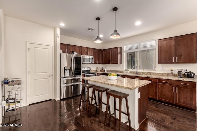 2149 E Aire Libre Ave, Phoenix, AZ 85022 - kitchen featuring appliances with stainless steel finishes, a kitchen bar, dark wood-type flooring, dark brown cabinets, and hanging light fixtures