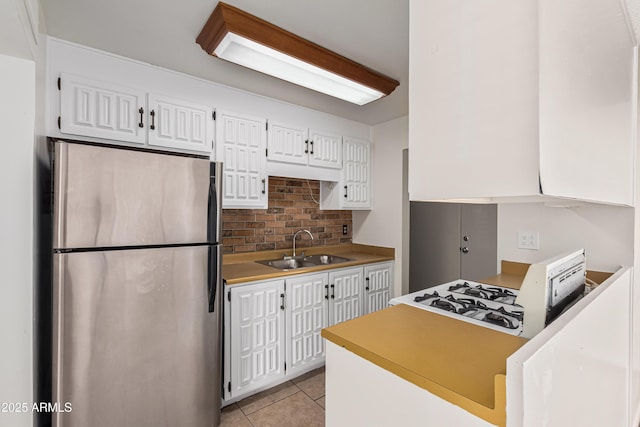 kitchen with light tile patterned flooring, stainless steel refrigerator, tasteful backsplash, sink, and white cabinets