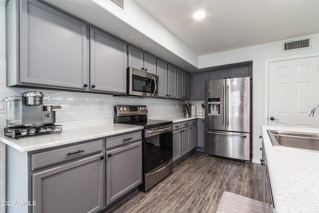 13709 W Rovey Ave, Litchfield Park, AZ 85340 - kitchen with stainless steel appliances, a sink, gray cabinets, dark wood-type flooring, and tasteful backsplash
