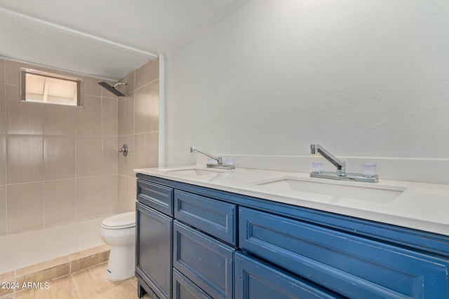 bathroom with tile floors, dual bowl vanity, toilet, and tiled shower