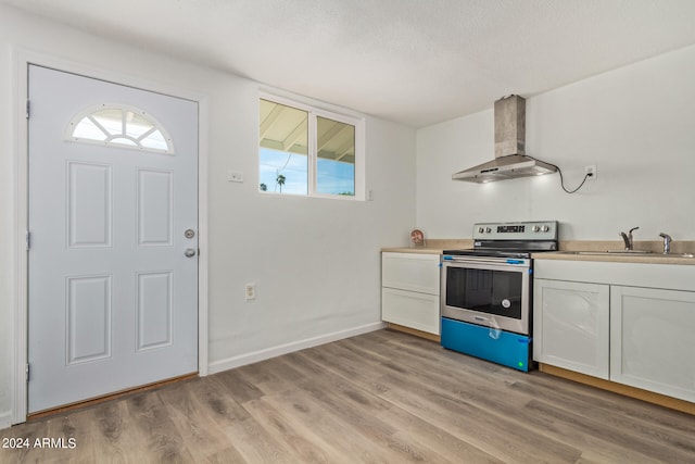 kitchen with wall chimney exhaust hood, sink, light wood-type flooring, white cabinetry, and electric range