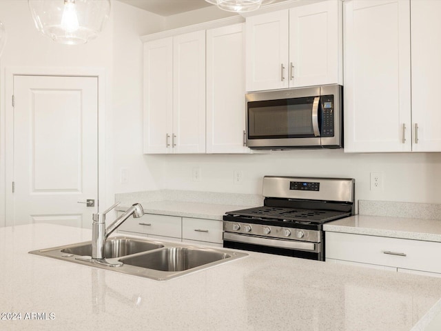 kitchen featuring hanging light fixtures, appliances with stainless steel finishes, sink, and white cabinets