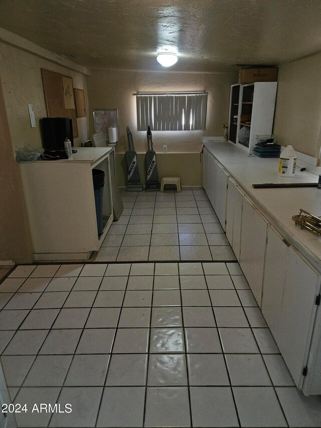 kitchen with a textured ceiling, light tile patterned flooring, and white cabinets