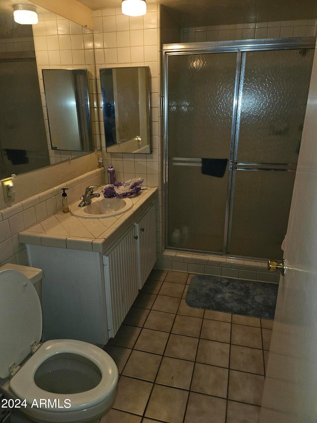 bathroom with toilet, tile patterned floors, walk in shower, tile walls, and vanity