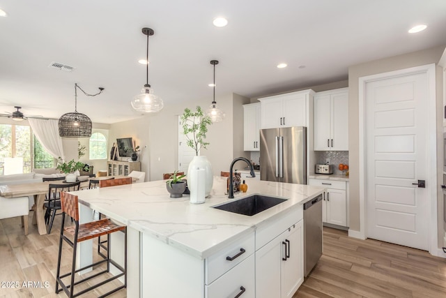 kitchen with stainless steel appliances, visible vents, decorative backsplash, a sink, and light wood-type flooring