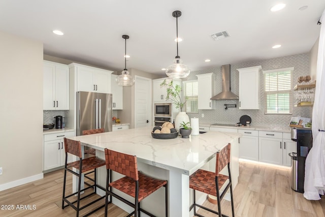 kitchen with a center island, visible vents, appliances with stainless steel finishes, white cabinets, and wall chimney range hood