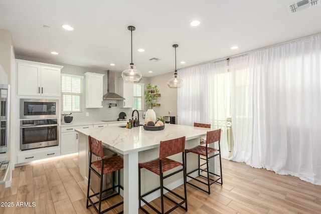 kitchen featuring a breakfast bar area, stainless steel appliances, visible vents, white cabinetry, and wall chimney range hood