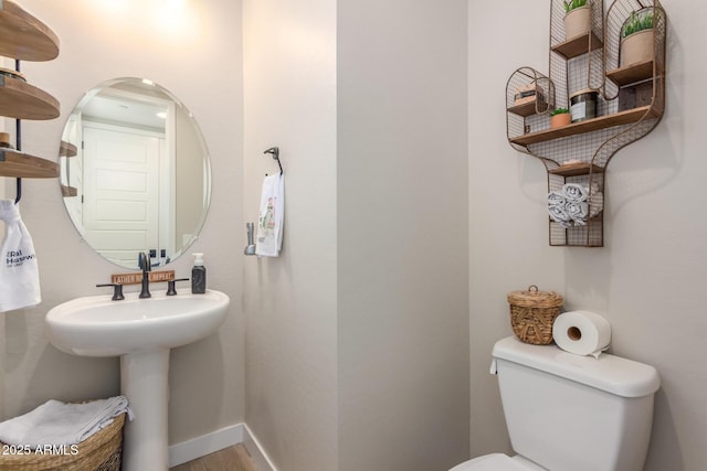 half bathroom featuring baseboards, a sink, toilet, and wood finished floors