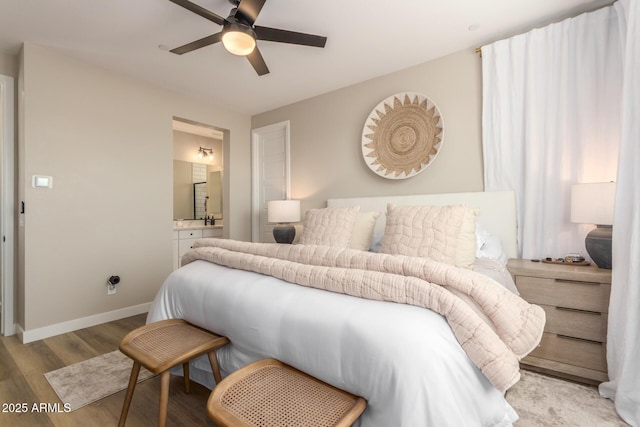 bedroom featuring a ceiling fan, ensuite bath, light wood-style flooring, and baseboards