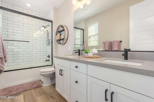 bathroom with double vanity, enclosed tub / shower combo, a sink, and wood finished floors