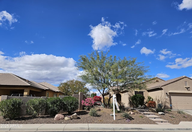 view of front facade with stucco siding, fence, a garage, driveway, and a tiled roof