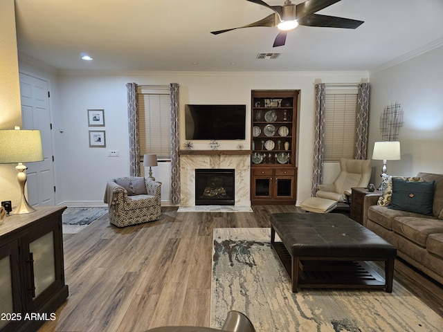 living room featuring hardwood / wood-style flooring, ceiling fan, a premium fireplace, and crown molding