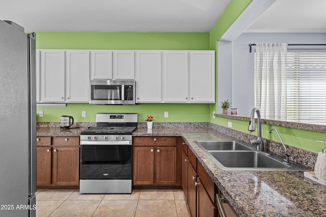 kitchen featuring brown cabinets, a sink, light tile patterned floors, white cabinets, and stainless steel appliances