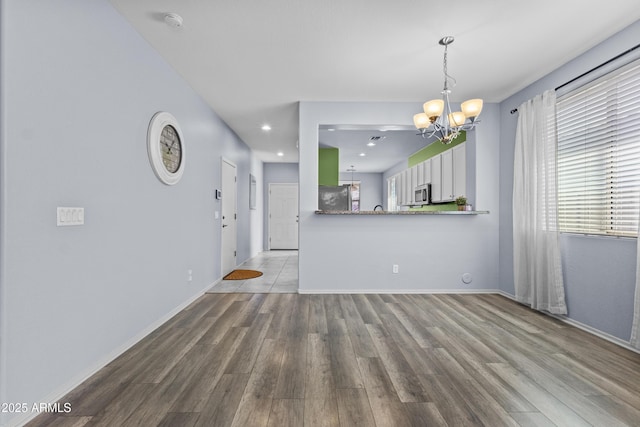unfurnished living room with recessed lighting, baseboards, an inviting chandelier, and wood finished floors