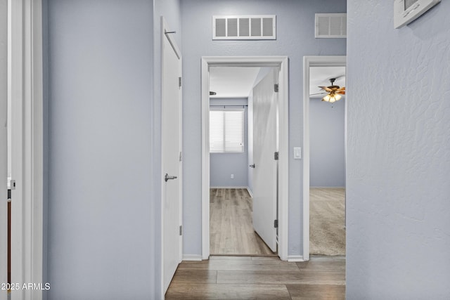 corridor featuring visible vents, baseboards, a textured wall, and wood finished floors