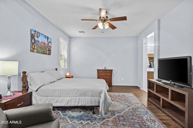 bedroom featuring a ceiling fan, visible vents, wood finished floors, baseboards, and ensuite bath