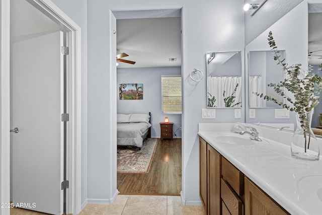 ensuite bathroom featuring double vanity, ceiling fan, a sink, baseboards, and connected bathroom