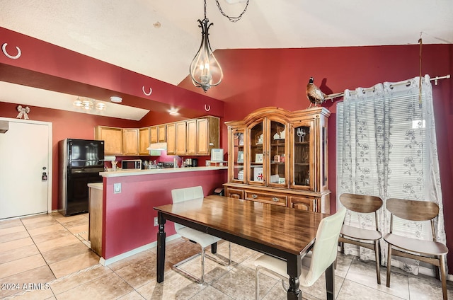 kitchen with kitchen peninsula, decorative light fixtures, vaulted ceiling, black refrigerator, and light tile patterned floors