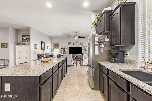kitchen with ceiling fan, dark brown cabinetry, freestanding refrigerator, open floor plan, and a kitchen island