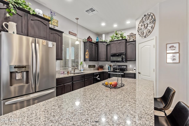 kitchen featuring visible vents, light stone countertops, dark brown cabinets, a kitchen breakfast bar, and appliances with stainless steel finishes