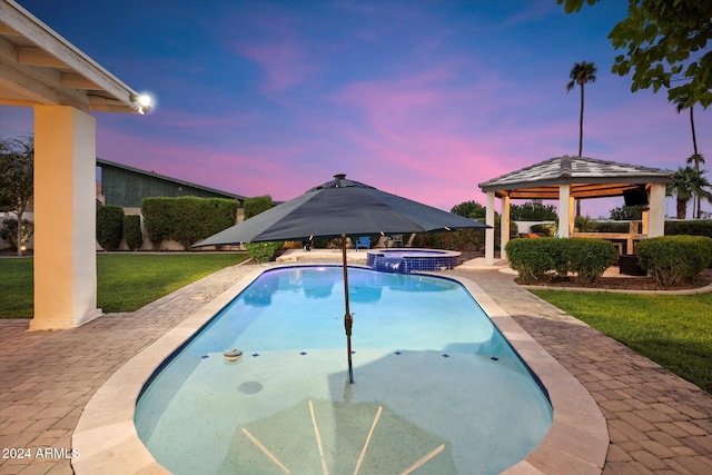 pool at dusk with a gazebo, a patio, an in ground hot tub, and a lawn